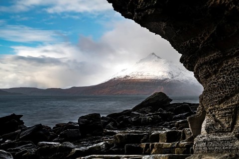 Big rocks in the water of the North Sea with snow-covered Cullin mountains in the background