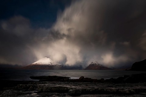 Big rocks in the water of the North Sea with snow-covered Cullin mountains in the background