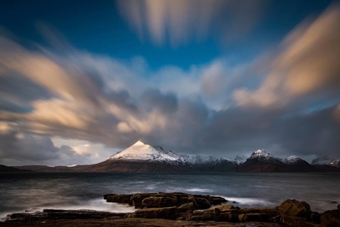 Big rocks in the water of the North Sea with snow-covered Cullin mountains in the background