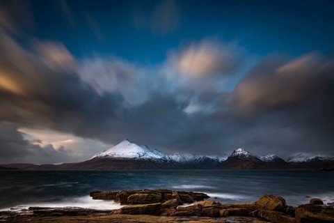 Big rocks in the water of the North Sea with snow-covered Cullin mountains in the background