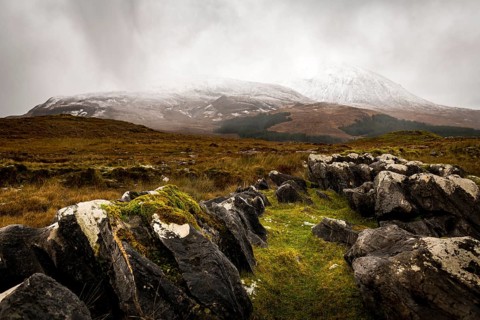 Dark rocks with white caps in Highland landscape with snow-covered Cullin mountains in the background