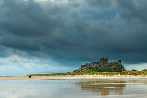Flat sandy coast with Bamburgh Castle and reflection in the water with dark clouds