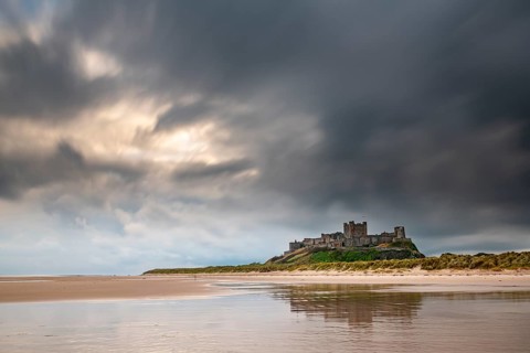 Flat sandy coast with Bamburgh Castle and reflection in the water with dark clouds