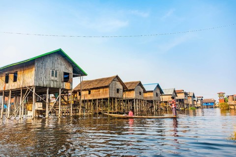 Wooden boat with locals in front of traditional stilt houses on Inle Lake