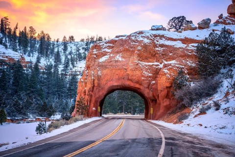 Road with tunnel through red rock arch in snow