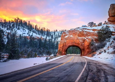 Road with tunnel through red rock arch in snow