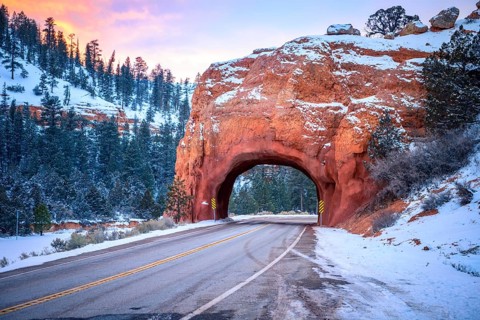 Road with tunnel through red rock arch in snow