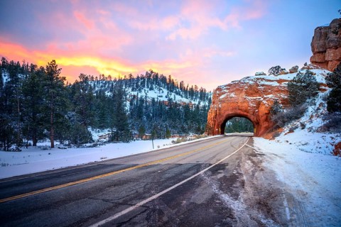 Road with tunnel through red rock arch in snow