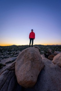 Young woman standing on round granite rocks at sunset