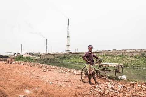 Worker with a rickshaw in front of a brickyard