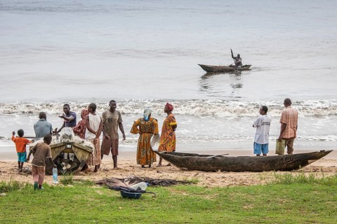 People standing near a dugout canoe on the beach