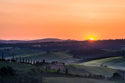 Typical green Tuscan landscape in Val d'Orcia with a farm on a hill