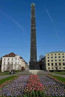 Obelisk with flower bed in front of houses roundabout