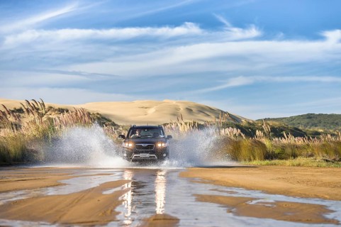 Black Hyundai Santa Fee 4x4 off-road vehicle driving through a streambed on approach to Ninety Mile Beach with sand dune behind