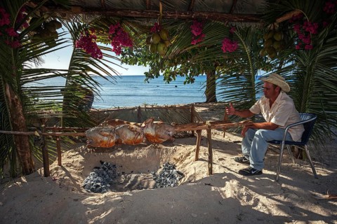Cuban man grilling turkeys and suckling pig at the beach of Playa Ancon