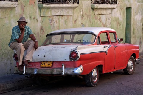 Cuban taxi driver sitting on a vintage taxi car
