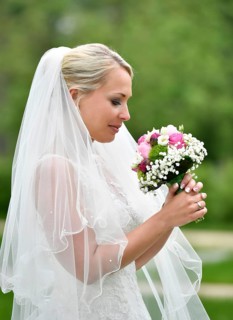 Bride in wedding dress with veil looking at bridal bouqet