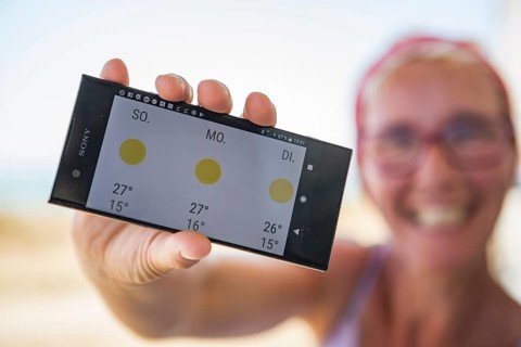Laughing woman on the beach happy about sunny weather in the weather forecast on her smartphone