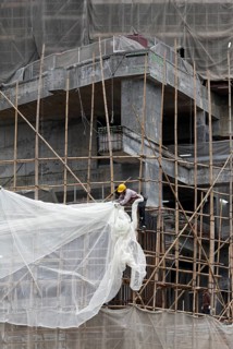 Workers attached a tarpaulin to a scaffolding of bamboo