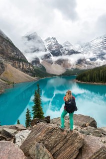 Young woman standing in front of a lake looking into mountain scenery
