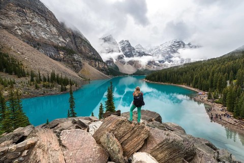 Young woman standing in front of a lake looking into mountain scenery
