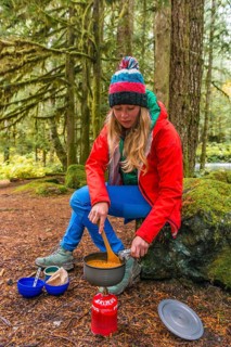 Young woman cooking outdoors with camping stove
