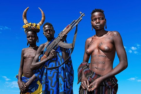 Young girls with decorative scars and man with Kalashnikov