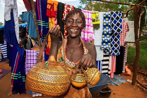 Laughing woman of the Hamer ethnic group sells artfully decorated calabashe pumpkins