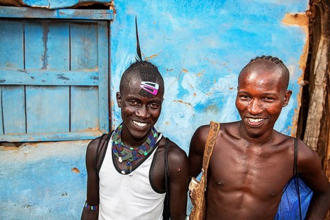 Laughing young men of the Hamer ethnic group with colorful hair clips and pearl jewelry
