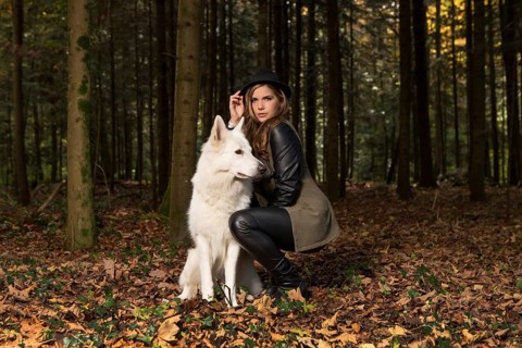 Blonde woman with white shepherd dog in the forest