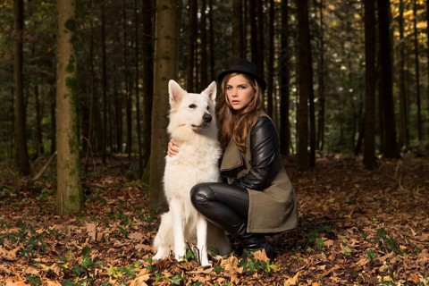 Blonde woman with white shepherd dog in the forest