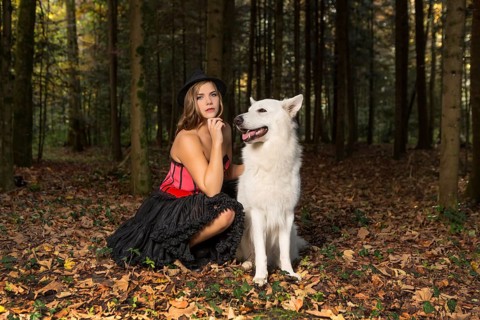 Blonde woman with white shepherd dog in the forest