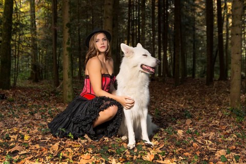 Blonde woman with white shepherd dog in the forest