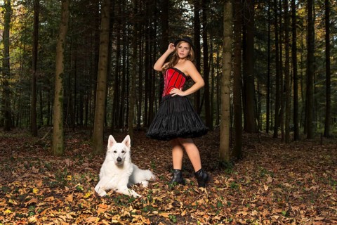 Blonde woman with white shepherd dog in the forest