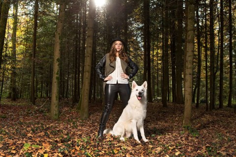 Blonde woman with white shepherd dog in the forest