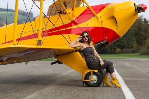 Young woman with sunglasses in overall and boots posing in front of double-decker airplane