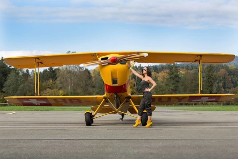 Young woman with sunglasses in overall and boots posing in front of double-decker airplane