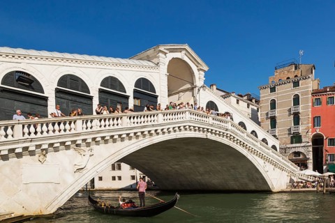 Tourists on Rialto bridge over Grand canal with traditional gondola