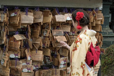 Woman dressed in traditional kimono looks at Ema wish plaques at Ueno Toshogu Shrine