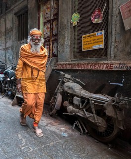 Hindu priest walks pass an abandoned motorcycle in the narrow streets
