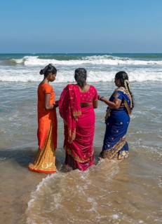 Three women in sari dress stand in ocean on the Bay of Bengal coast
