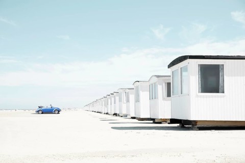 Blue VW Beetle cabriolet faces white beach huts