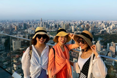 Three young Chinese tourists with hats on the viewing platform of the Maha Nakhon Tower