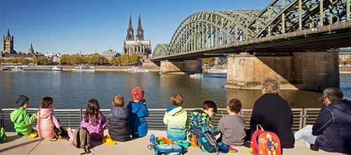 Children's group having a picnic on the Rhine Boulevard with Cologne Cathedral and Hohenzollern Bridge in the background