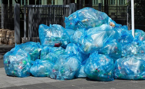 Full light blue garbage bags with plastic garbage on one heap