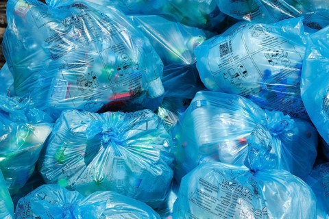 Full light blue garbage bags with plastic garbage on one heap