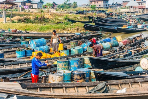Men working in wooden boats with old oil barrels in the harbor
