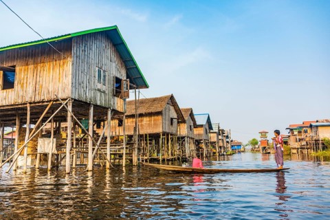 Wooden boat with locals in front of traditional stilt houses on Inle Lake