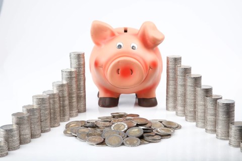 Piggy bank behind heaped and stacked coins