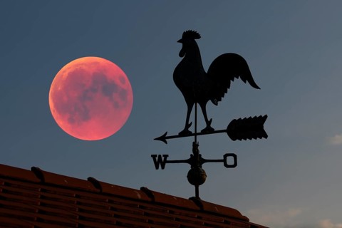 Blood moon over the roof of a house with weather vane with weather cock